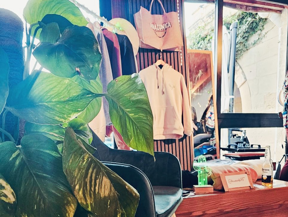 Amazonica studio display with hanging hoodies, tote bag, and green plant styling