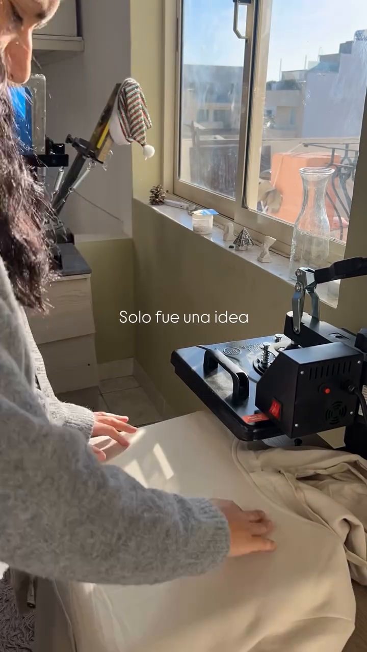 Person preparing a garment on a heat press near a studio window